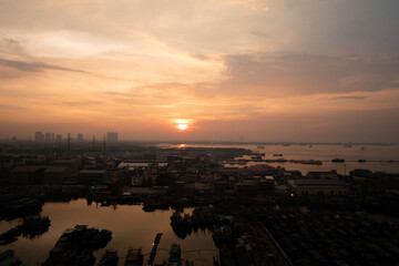Fototapeta premium A vibrant sunset over Jakarta, with warm orange and red hues reflecting on the water, creating a dramatic and serene atmosphere.