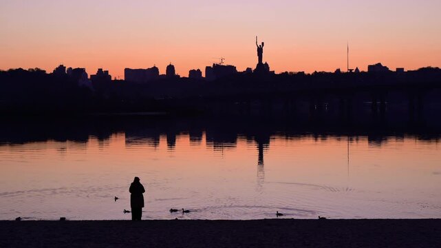 Kyiv cityscape reflecting in dnipro river at sunset with mother ukraine monument