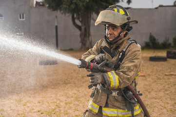 Brave firefighter behind a curtain of water standing in an epic pose putting out a fire.