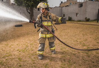 Brave firefighter behind a curtain of water standing in an epic pose putting out a fire while calling his colleagues.