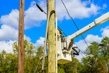 Workers use crane truck from bucket lift to conduct maintenance on power lines against backdrop...