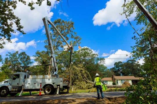 Workers operate bucket truck to repairs power lines in suburban neighborhood after storm.
