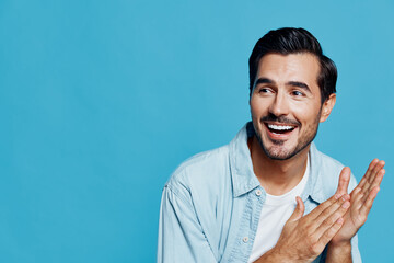 Happy smiling young man with short hair wearing a light blue shirt, sitting against a solid blue...