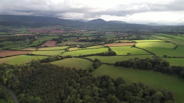 Green fields and meadows split by paths and draws. Aerial panoramic footage of countryside. Overcast sky. Wales, UK