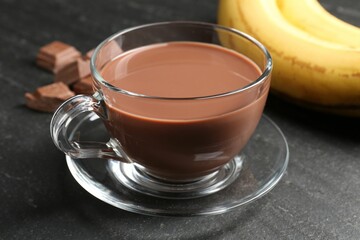 Tasty chocolate milk in glass cup, pieces and bananas on black table, closeup