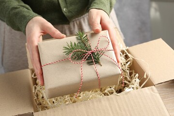 Woman packing gift into parcel box at table, closeup