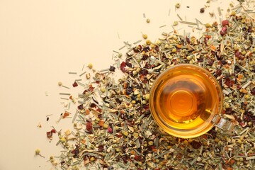 Delicious herbal tea in glass cup and dry leaves on beige background, top view. Space for text