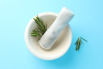 Ceramic mortar with rosemary and pestle on light blue background, top view