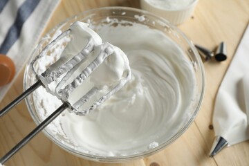 Hand mixer with whisks and bowl of whipped cream on wooden table, above view