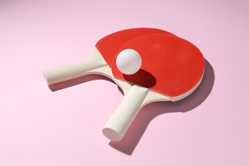 Ping pong rackets and ball on pink background, closeup