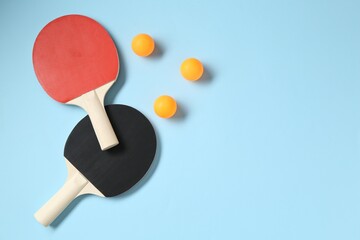 Ping pong rackets and balls on light blue background, flat lay. Space for text