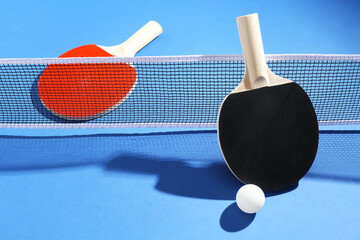 Ping pong rackets, ball and net on blue background