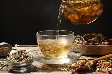 Pouring herbal tea from teapot into cup at wooden table, closeup. Space for text