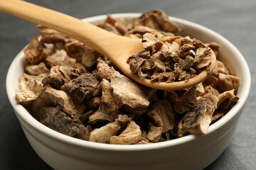 Pieces of dry chicory roots in bowl and spoon on dark table, closeup