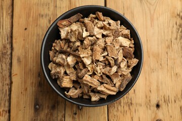 Pieces of dry chicory roots in bowl on wooden table, top view