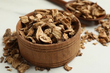 Pieces of dry chicory roots in bowl and spoon on white table, closeup