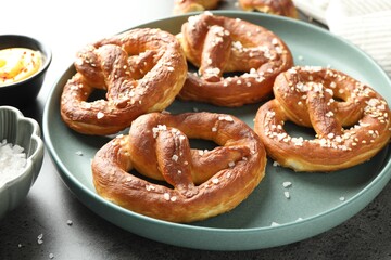 Tasty pretzels with salt and sauce on grey table, closeup