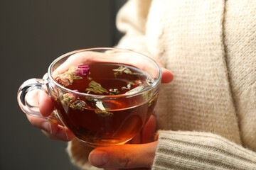 Woman with glass cup of aromatic herbal tea on grey background, closeup