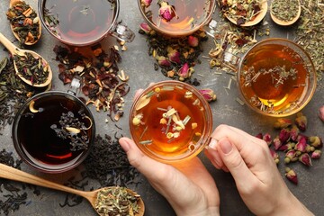 Woman with aromatic herbal tea, dry leaves and flowers at grey table, top view