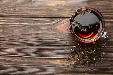 Aromatic herbal tea in glass cup and dry leaves on wooden table, flat lay. Space for text
