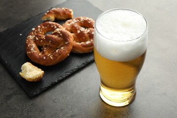 Tasty pretzels and glass of beer on dark textured table, closeup