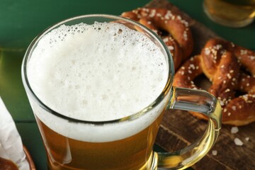 Glass of beer and tasty pretzels on green table, selective focus