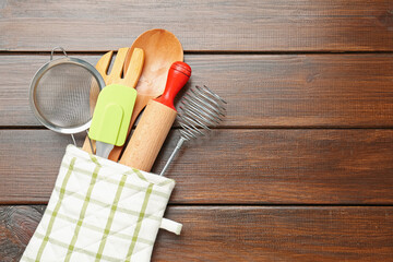 Different kitchen utensils in oven mitten on wooden table, top view. Space for text
