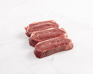 Fresh raw beef steaks arranged on a white marble surface close up – High Resolution Raw Meat Image for Food Industry or Food Packaging