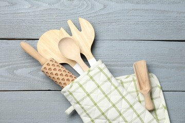 Different kitchen utensils in oven mitten on light grey wooden table, top view