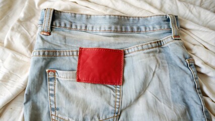 A red label with stitching sewn to the back pocket of blue denim jeans resting on a white cloth