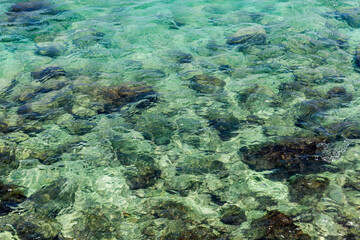 Transparent, crystal-clear emerald water with visible rocks beneath the rippled surface, reflecting sunlight in a tranquil seascape. Clean and smooth texture. Koh Lipe, Thailand.
