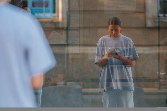 young woman with cell phone reflected in street shop window