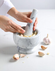 Garlic cloves being crushed with a stone mortar and pestle on a marble countertop.