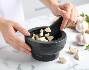 Garlic cloves being crushed with a stone mortar and pestle on a marble countertop.