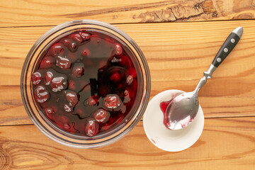 Cherry sweet jam in a glass plate on a wooden table, top view, close-up.