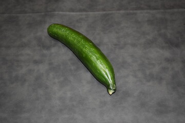 one whole green fresh cucumber on a black slate
