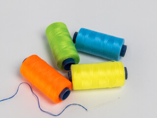 Colorful spools of thread with a sewing needle on a bright white background