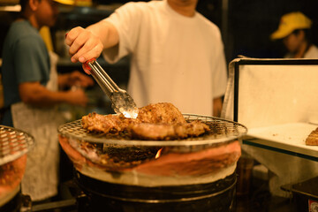 A vendor grills seasoned pork over a traditional charcoal stove at a lively night market