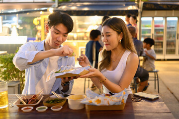 Two friends enjoy street food at a night market, squeezing fresh lime over Pad Thai to enhance the flavor in a lively, outdoor dining atmosphere