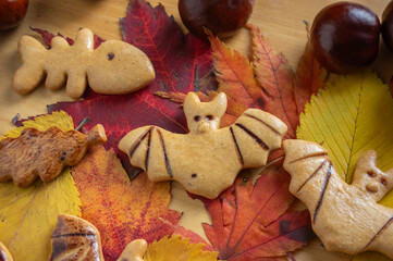 Decorated gingerbread cookies for Halloween celebration spread on table with colorful autumnal leaves and chestnut fruit
