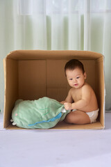 a baby sitting in a cardboard box on a white surface, with a green cloth draped over it and a white...