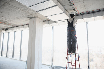 Construction worker installing ventilation system on a ladder in building under construction