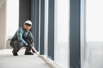 Construction worker applying sealant to window frame in modern building