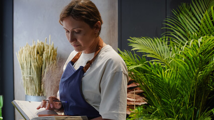 The florist is talking on the phone and writing down business notes in a notebook. Small business. Close-Up.