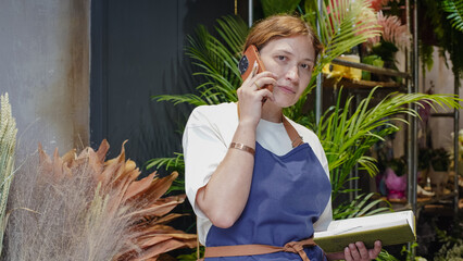 The florist is talking on the phone, smiling, and writing down business notes in a notebook. Small business. Close-Up.