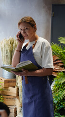 The florist is talking on the phone, and writing down business notes in a notebook. Small business. Close-Up.