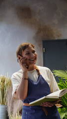 The florist is talking on the phone, smiling, and writing down business notes in a notebook. Small business. Close-Up.