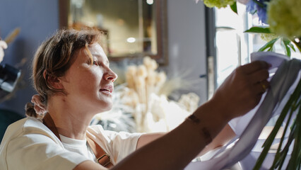 Florist conducts online training on creating bouquets using a phone. Florist records instructional video while looking into the camera. Small business.  Close-Up.