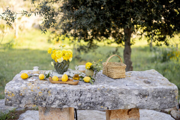 Close-up of a rustic stone table styled with bright yellow ranunculus flowers, fresh lemons with...