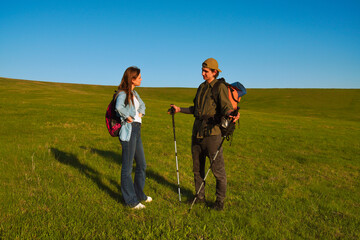 Young Couple Hiking with Trekking Poles in Open Green Field
